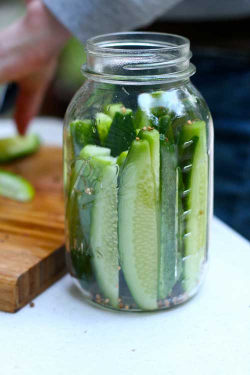 Pickles spears in a mason jar, with no brine. A wood cutting board runs out of the left edge of the image.