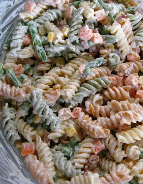 Tri-colored spiral pasta in a glass bowl. The pasta is covered in a mayonnaise based dressing.