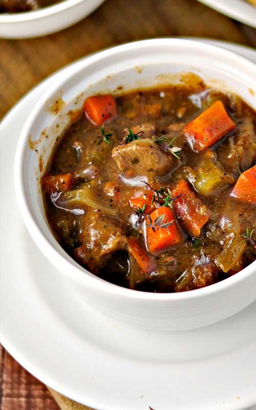 A white bowl filled with Classic Beef Stew. Chunks of carrot, potato, and beef covered in gravy are visible.